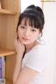 A young woman leaning against a bookshelf with her hand on her chin.