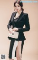 A woman in a black and white suit holding a white purse.