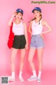 Two young women standing next to each other on a pink background.