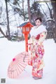 A woman in a kimono standing in the snow holding an umbrella.