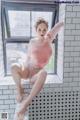 A woman in a pink bodysuit sitting on a window sill.