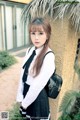 A woman in a school uniform leaning against a wall.