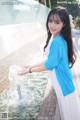 A woman in a blue and white dress standing next to a fountain.