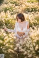 A woman in a white lingerie sitting in a field of tall grass.