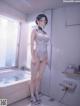 A woman in a white bodysuit standing in a bathroom next to a bathtub.