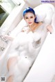 A woman with blue hair is taking a bath in a bathtub.