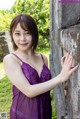 A woman in a purple lingerie leaning against a stone wall.